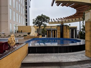 Un'area piscina esterna moderna con un design circolare, circondata da un muretto basso e un pergolato.