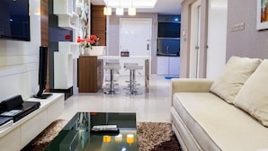 A modern living room with a sofa, a coffee table, and a TV. There is a kitchen area with a dining table and chairs. - Furnished 1BR City View Casa Grande Apartment (Jakarta)