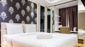 A large bed with white bedding, a dark patterned wall, and a sliding door leading to a bathroom. - Furnished 1BR City View Casa Grande Apartment (Jakarta)