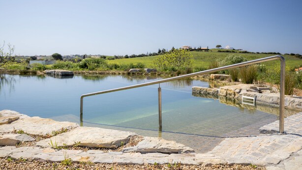A clear outdoor pool with a metal railing, surrounded by stone tiles and greenery. - F - Casa do Garibaldi in Quinta das Alagoas by DreamAlgarve (Lagos)