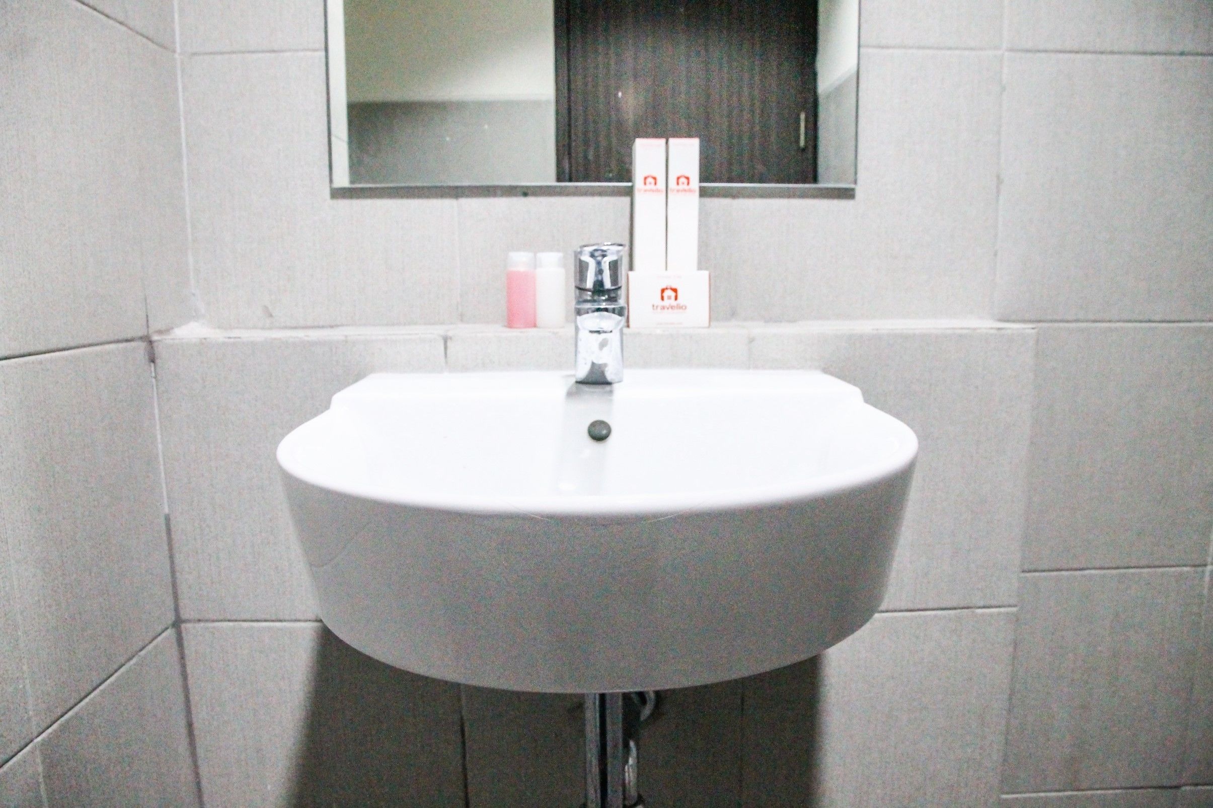 A white bathroom sink with a mirror above it, two boxes labeled 'travelio' on the wall, and a bottle of soap on the counter.
