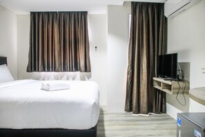 Ett hotellrum med en säng, en tv på ett stativ och ett litet kylskåp.