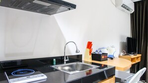 A compact kitchen with a built-in induction cooktop, a stainless steel sink, and a compact refrigerator. - Cozy Studio Room Bintaro Icon Apartment (South Tangerang)