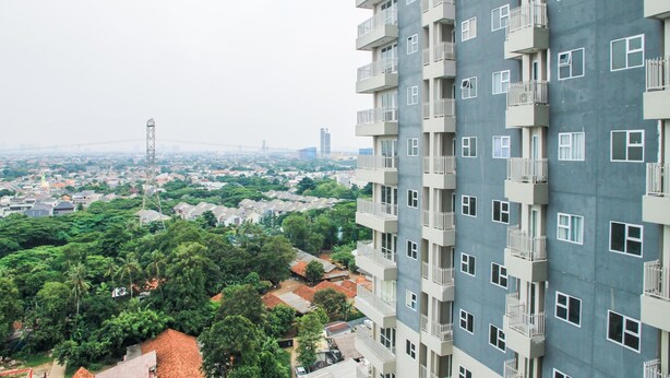 A high-rise residential building with multiple balconies, a dense urban background, and a mix of greenery and residential structures. - Cozy Studio Room Bintaro Icon Apartment (South Tangerang)