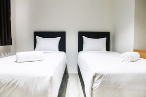 Two single beds with black headboards and white bedding, set against a light-colored floor and simple design.