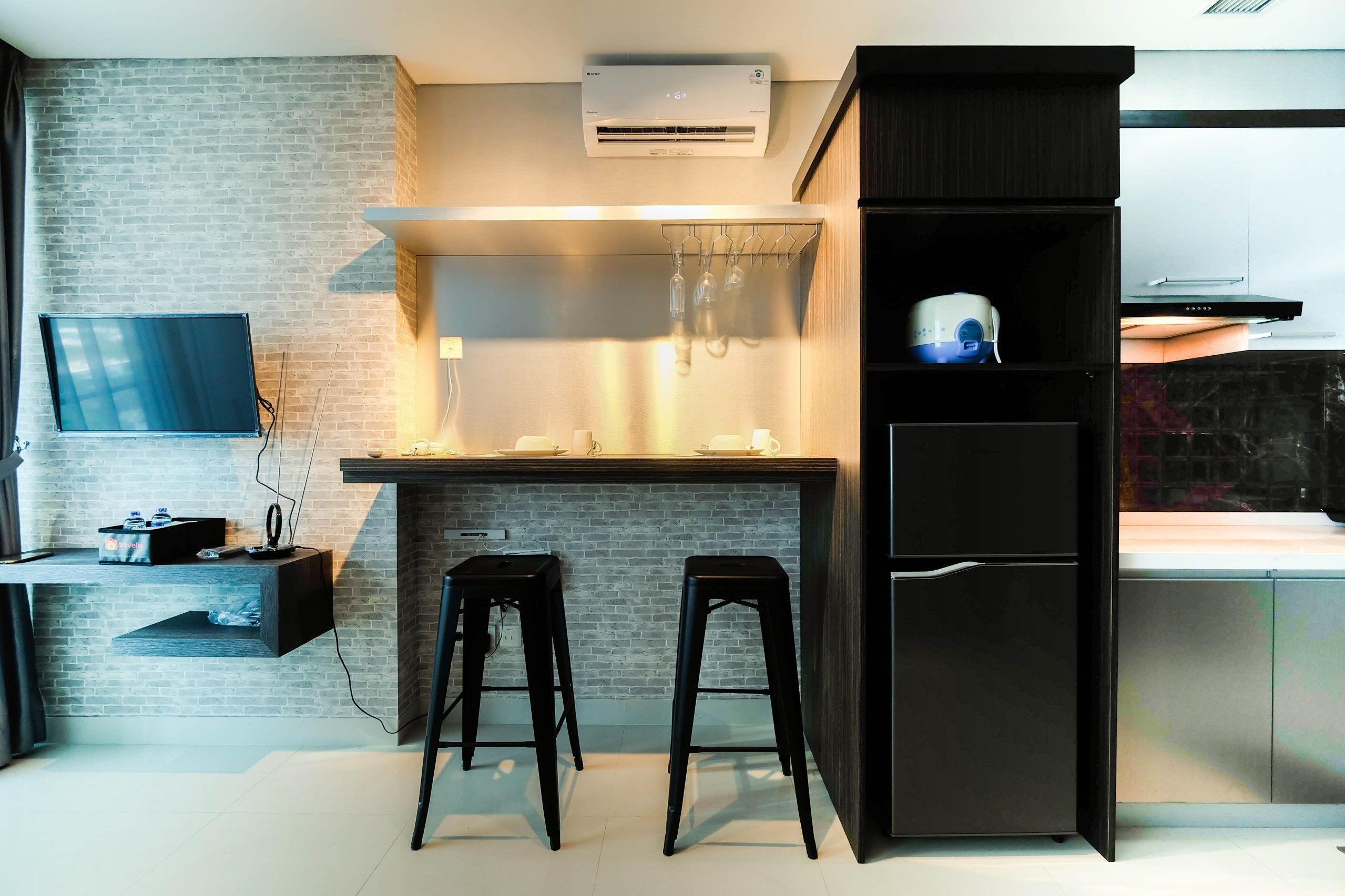 A modern kitchen with a brick wall, a flat-screen TV, a built-in oven, and two bar stools.