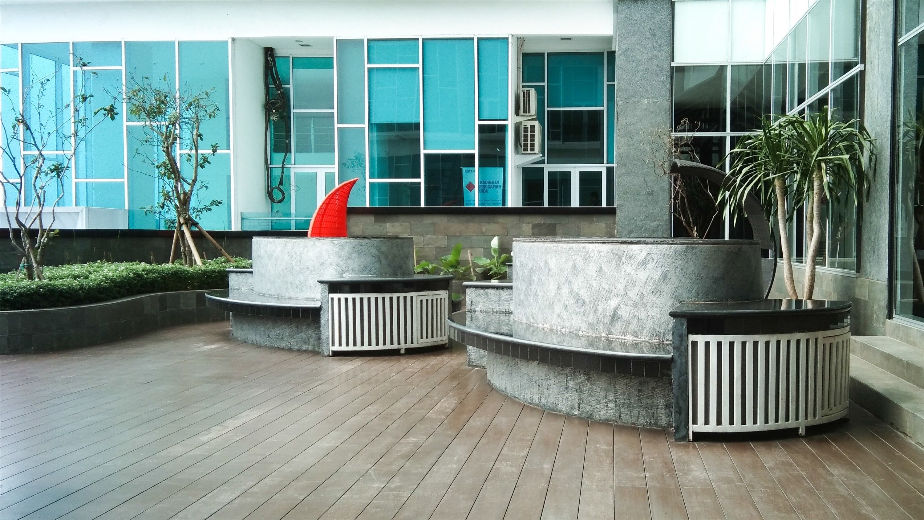 Een modern buitengebied met ronde plantenbakken, een rode sculptuur en een gebouw met grote ramen op de achtergrond.