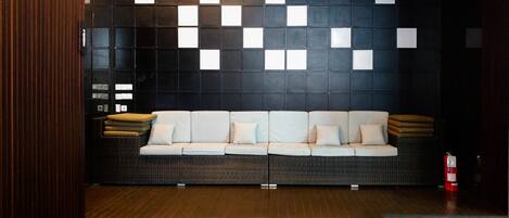 Ein modernes Interieur mit einer dunklen Wand, die ein geometrisches Muster aus weißen Quadraten zeigt, einer hellen Couch mit Kissen und einem Holzboden.