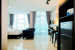 Quarto de hotel moderno com cama, sofá, televisão, frigorífico e área de cozinha.
