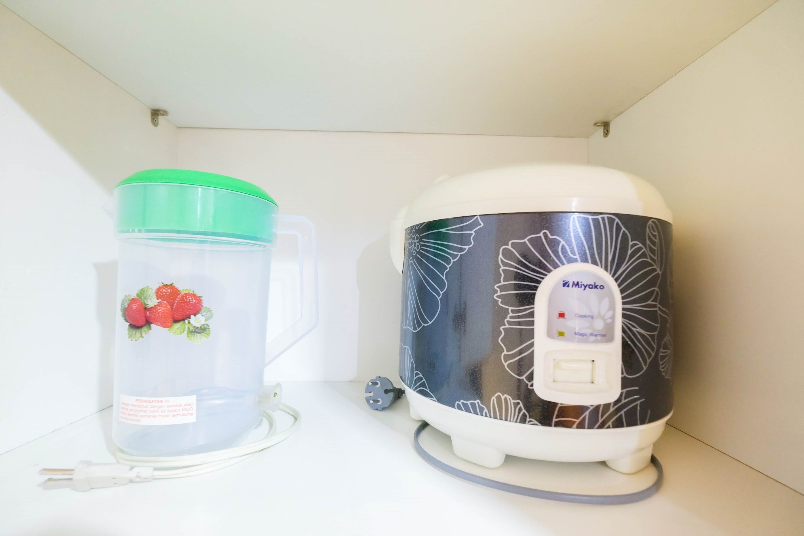 Two kitchen appliances, a water dispenser with a green lid and a rice cooker with a floral design.