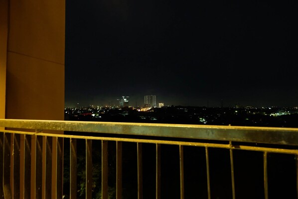A nighttime cityscape viewed from a balcony with a metal railing.
