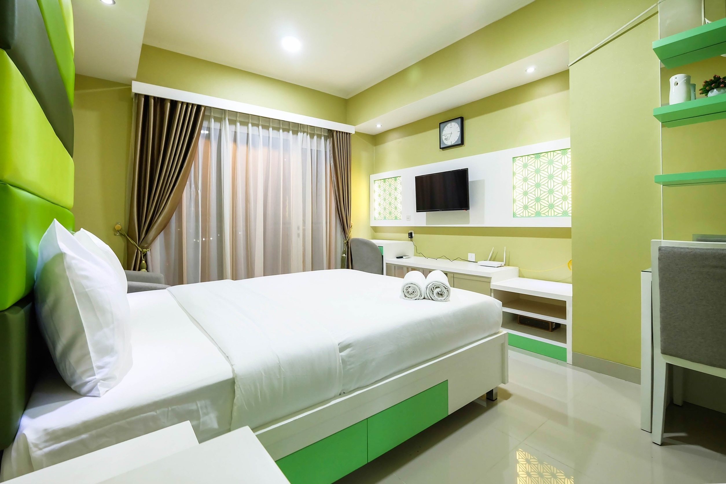A hotel room with a bed, a TV, a desk, and a shelf.