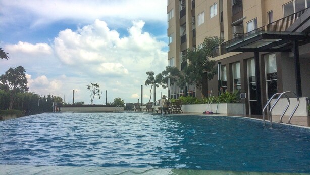 A swimming pool adjacent to a multi-story building with balconies. - Strategic Studio The Oasis Cikarang near Omni Hospital (Cikarang)