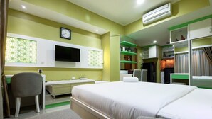 A hotel room with a bed, a desk, a chair, a TV, and a kitchenette. - Strategic Studio The Oasis Cikarang near Omni Hospital (Cikarang)