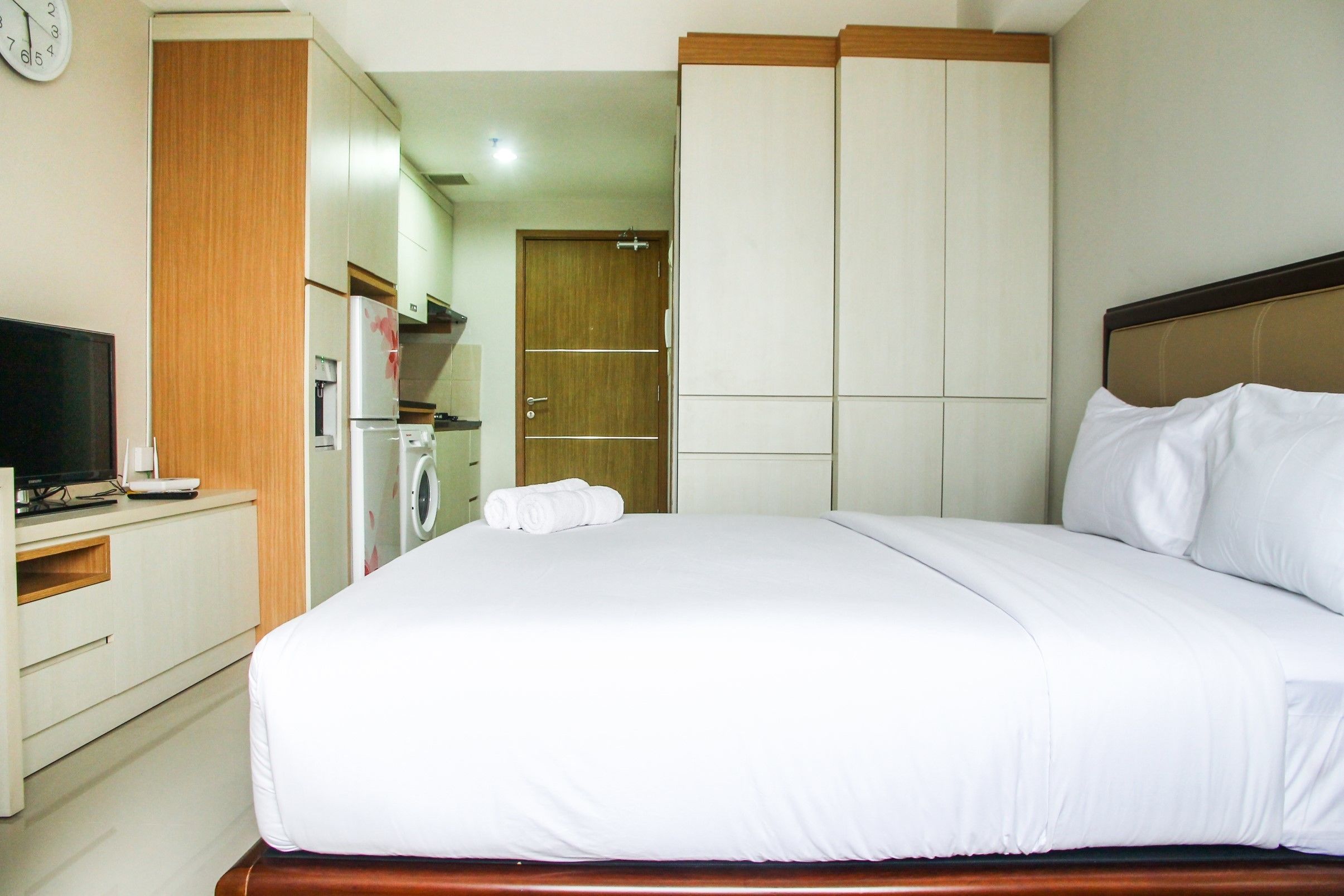 A hotel room with a large bed, a wooden headboard, a flat-screen TV, a wardrobe, and a door leading to a bathroom.