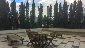 An outdoor seating area with a checkered floor, surrounded by tall trees and a tall building in the background.