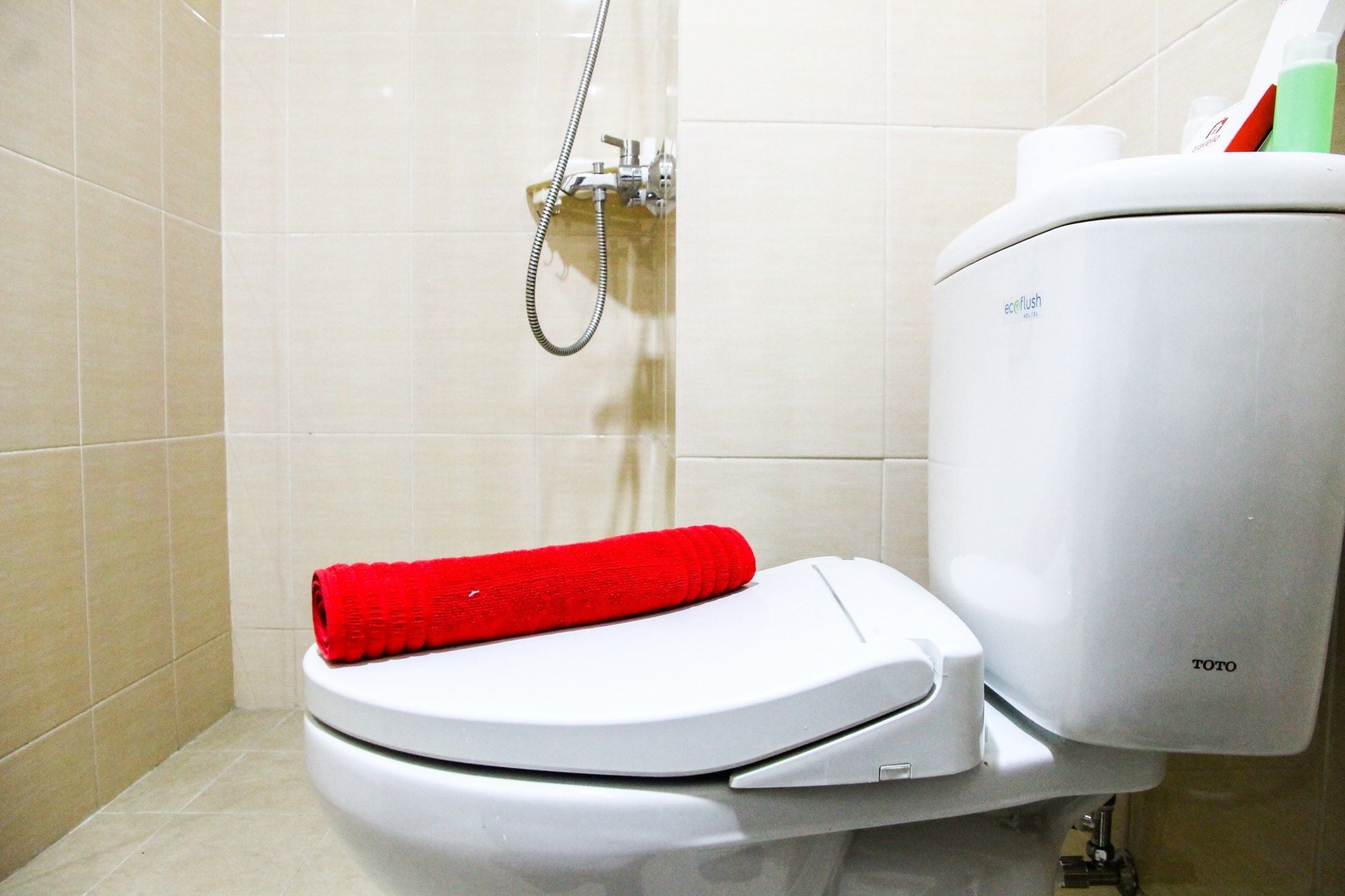 A modern toilet with a white seat and lid, a red towel on the seat, and a visible toilet paper holder.