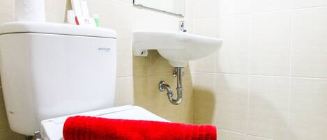 A bathroom with a toilet, a sink, and a red towel on the seat.