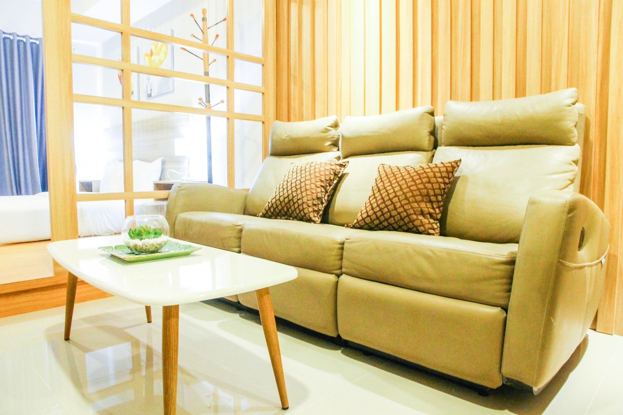 Una sala de estar moderna con un sofá color crema, una mesa de centro blanca y un amplio ventanal con persianas.