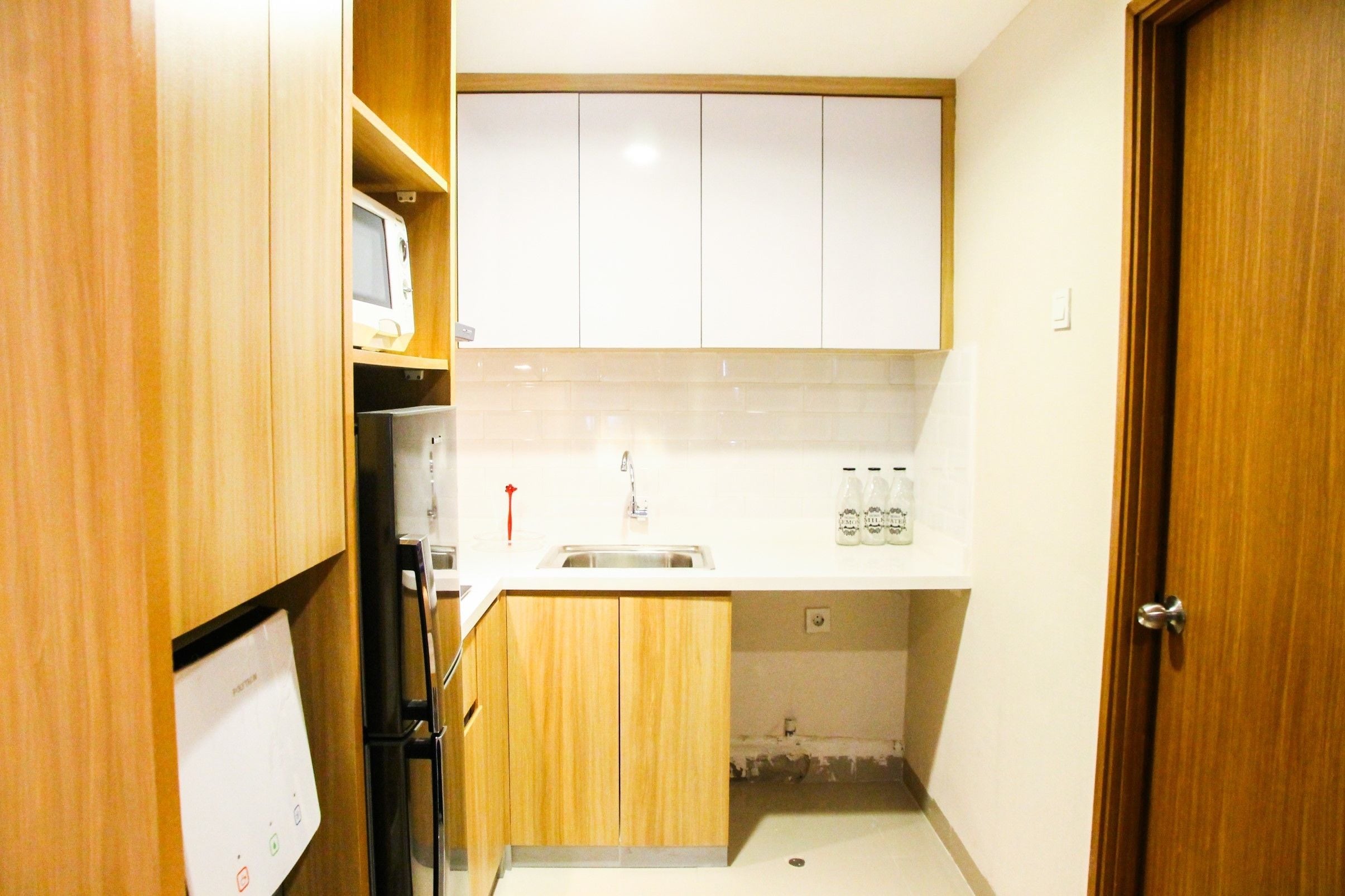 Una cucina compatta con mobili in legno, un forno a microonde integrato, un lavello e un piano di lavoro con bottiglie.