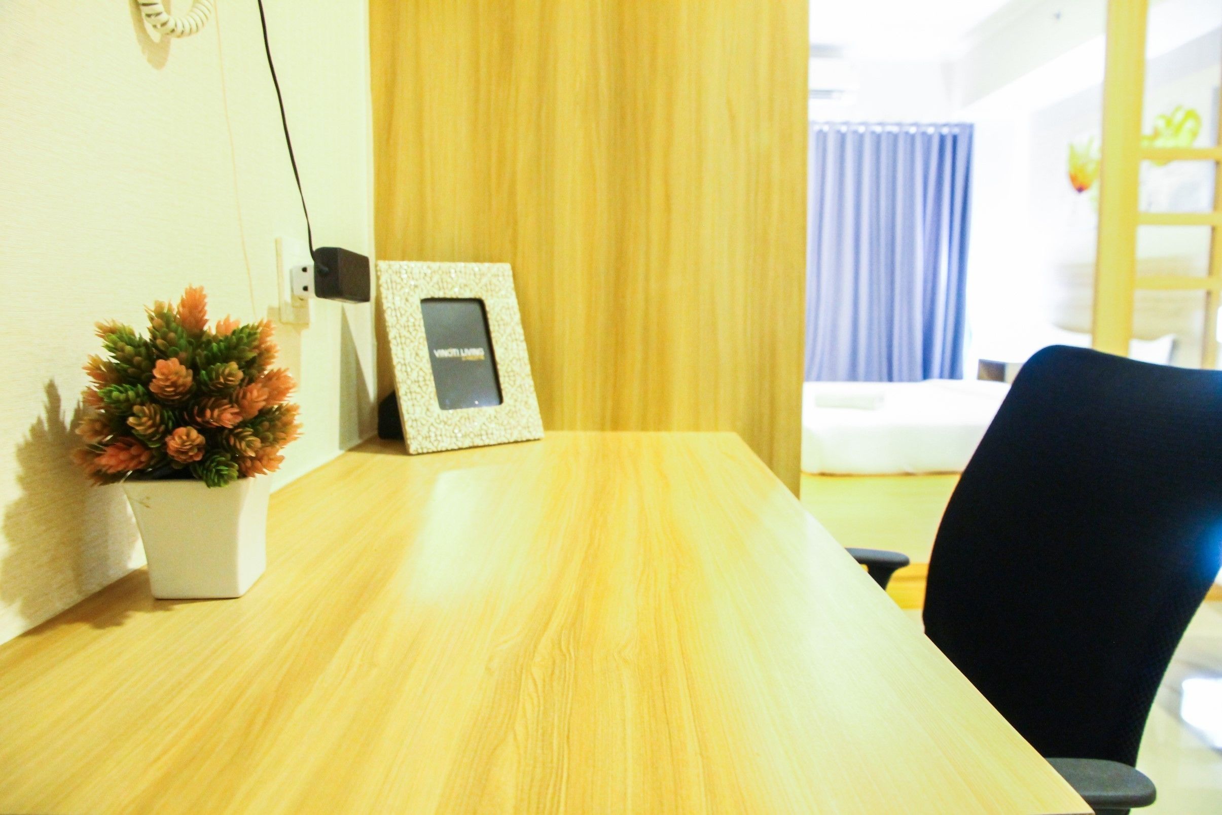 A wooden table with a framed picture, a potted plant, and a black office chair in a room with a wooden door and a window with curtains.