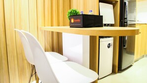 Une cuisine compacte dotée de meubles en bois, d’un petit réfrigérateur et d’une table décorée sur le thème du voyage, agrémentée d’une plante.