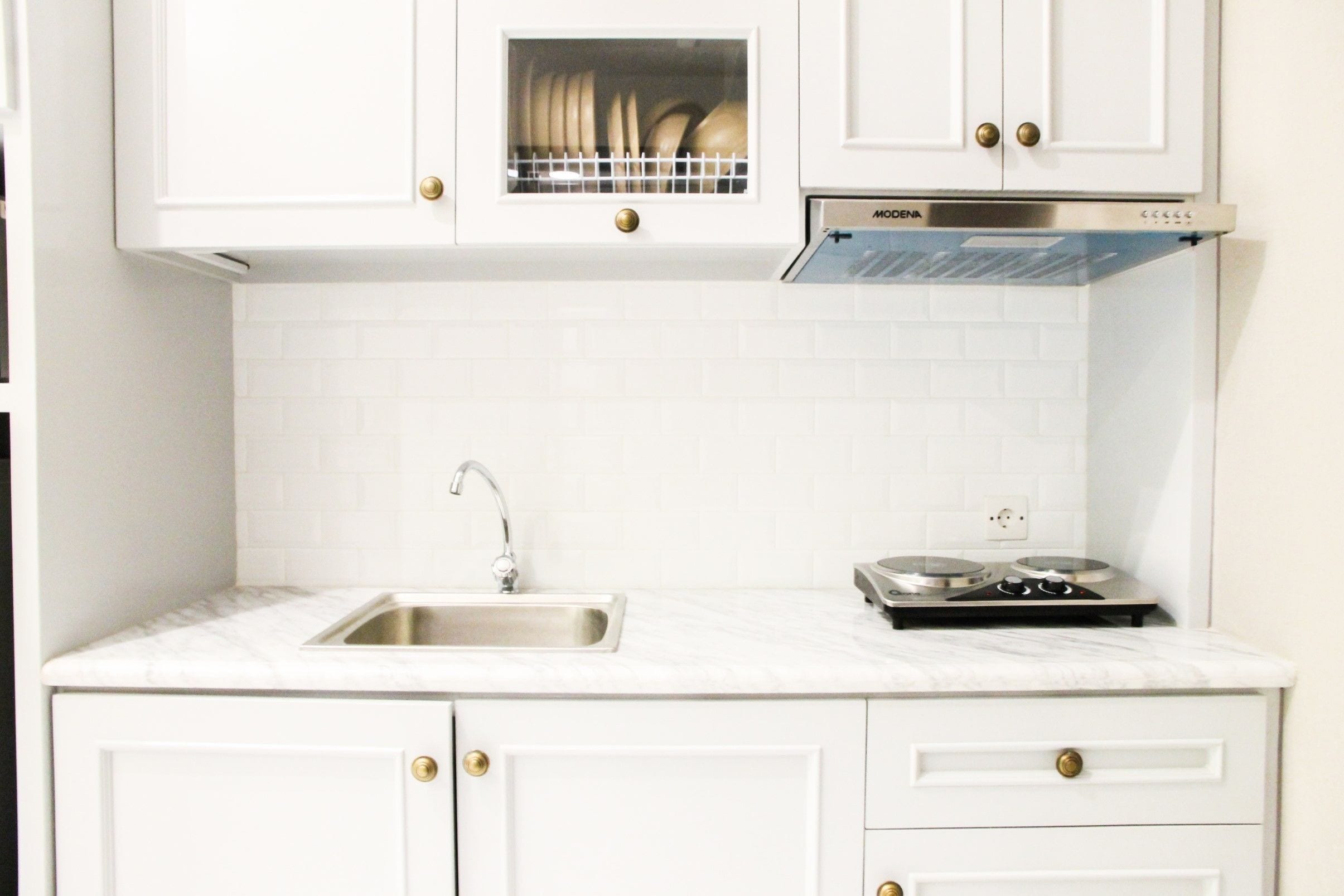 A kitchen with white cabinets, a stainless steel sink, a dish rack, and a stove.