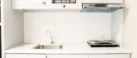 A kitchen with white cabinets, a stainless steel sink, a dish rack, and a stove.