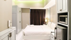 A hotel room with a bed, a desk, a microwave, and a wardrobe. - Studio Room with City View Casa De Parco Apartment (Pagedangan)