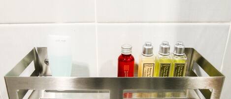 Una repisa metálica con cuatro frascos de artículos de tocador frente a una pared de azulejos blancos.