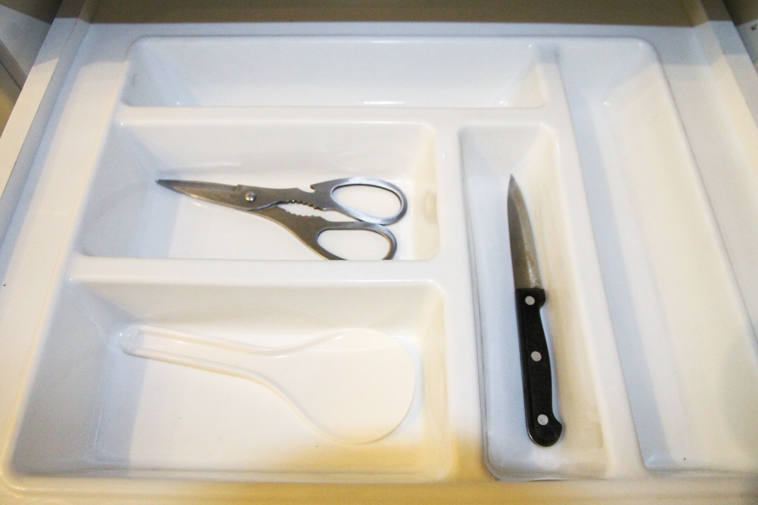 Eine Schublade mit Fächern, die eine Schere, ein Messer und einen Löffel enthalten.