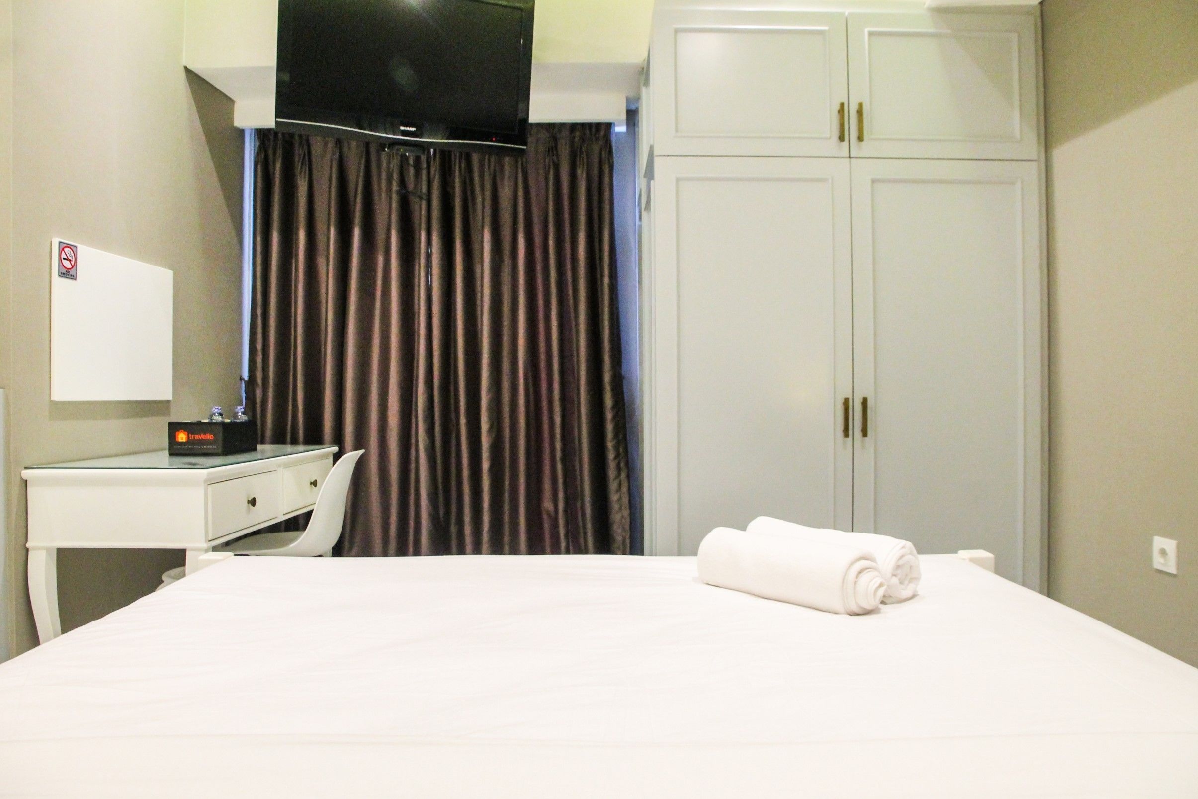 A hotel room with a bed, a desk with a television, a wardrobe, and a curtain.