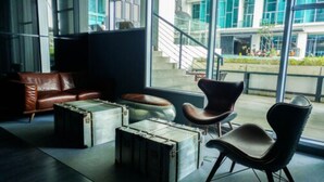 A modern lounge area with leather furniture, a staircase, and large windows.