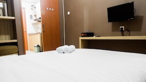 A hotel room with a bed, a TV mounted on the wall, and a wooden shelf with a remote control.