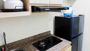 A kitchen with a gas stove, a black refrigerator, and a kettle on a shelf.