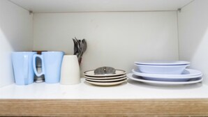 A white shelf with stacked plates, bowls, and a set of utensils.