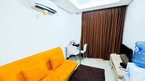 A room with a bright orange sofa, a small table with a chair, a water dispenser, and a large window with curtains. - 1BR Sky Terrace Lagoon Condo Apartment near Daan Mogot Mall (Jakarta)