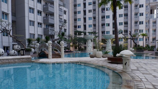A swimming pool with a fountain, surrounded by palm trees and decorative elements. - 1BR Sky Terrace Lagoon Condo Apartment near Daan Mogot Mall (Jakarta)