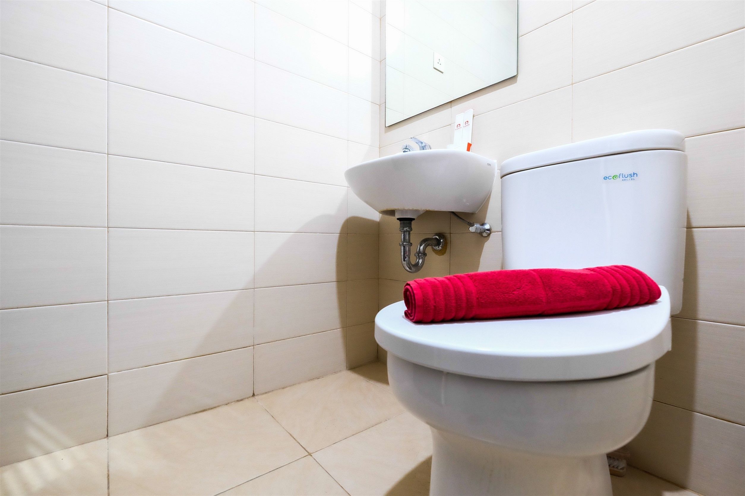 A bathroom with a white toilet, a sink, and a red towel on the toilet seat.