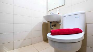 A bathroom with a white toilet, a sink, and a red towel on the toilet seat.