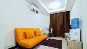 A compact living space with a sofa, a small table, a water dispenser, and a ceiling light. - 1BR Sky Terrace Lagoon Condo Apartment near Daan Mogot Mall (Jakarta)