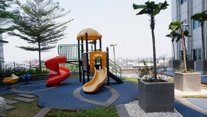 A playground with slides and a climbing structure, surrounded by landscaped areas and palm trees. - 1BR Sky Terrace Lagoon Condo Apartment near Daan Mogot Mall (Jakarta)