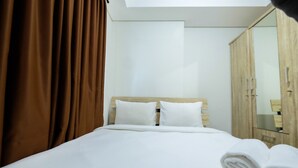 A hotel room with a bed, white bedding, a wooden headboard, a wardrobe, and a mirror. - 1BR Sky Terrace Lagoon Condo Apartment near Daan Mogot Mall (Jakarta)