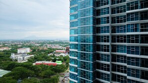A high-rise building with a modern glass facade, surrounded by greenery and other buildings. - Well Equipped 1BR Brooklyn Alam Sutera Apartment near IKEA (South Tangerang)