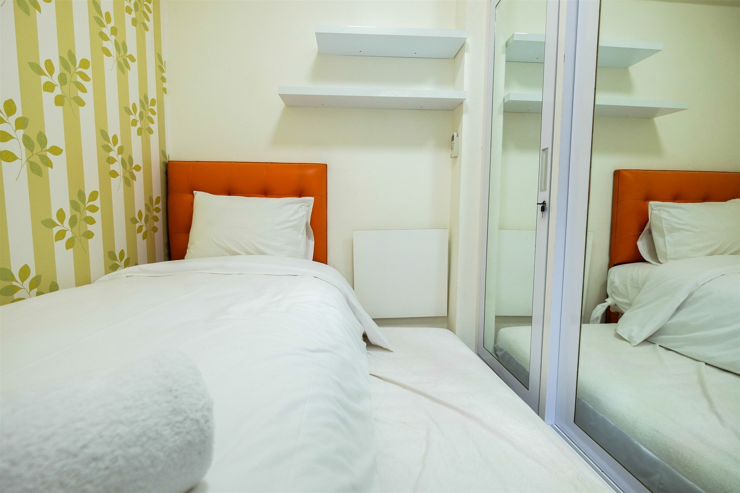 A hotel room with two beds, white bedding, an orange headboard, a radiator, and a glass door.