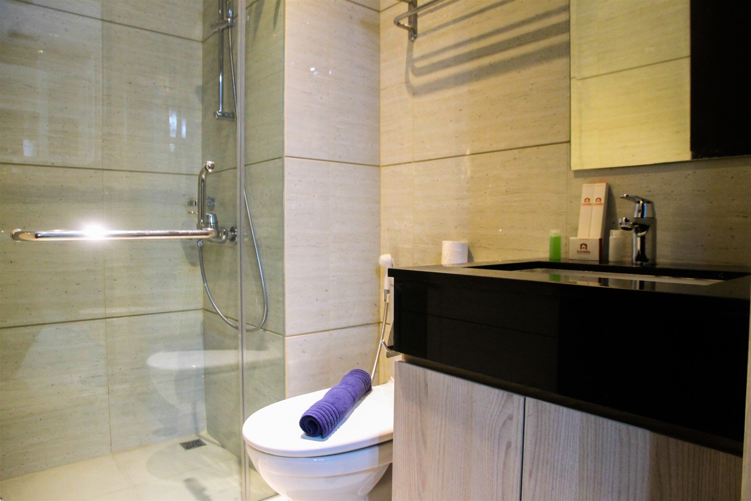 A modern bathroom with a glass shower enclosure, a white toilet, and a black countertop with a wooden cabinet.