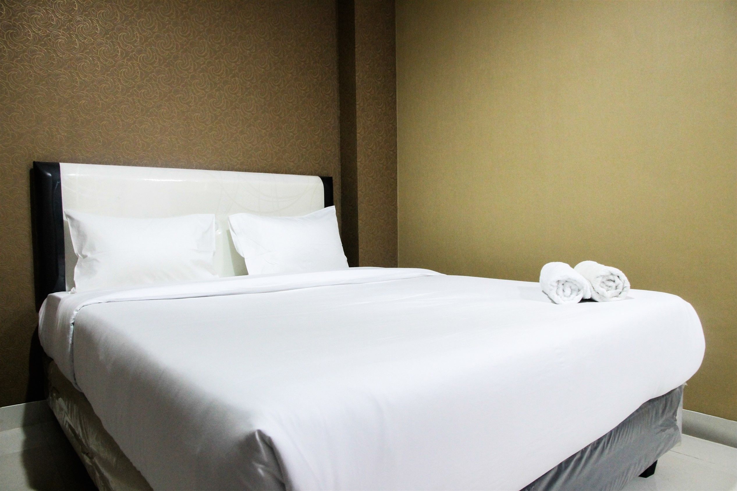 A neatly made bed with white linens and a rolled towel on top, set against a patterned wall.