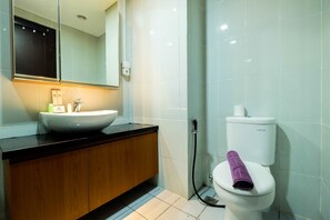 A modern bathroom with a white sink, wooden vanity, and a toilet with a purple towel. - Exclusive 1BR Casa De Parco Apartment near AEON Mall (Pagedangan)