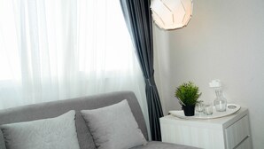 A modern bedroom with a grey sofa, a bedside table with a plant, and a white nightstand. - Sophisticated Studio at The Oasis Apartment (Cikarang)