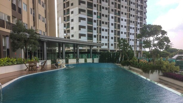 A swimming pool with a lounge area, surrounded by a modern building with multiple floors and balconies.